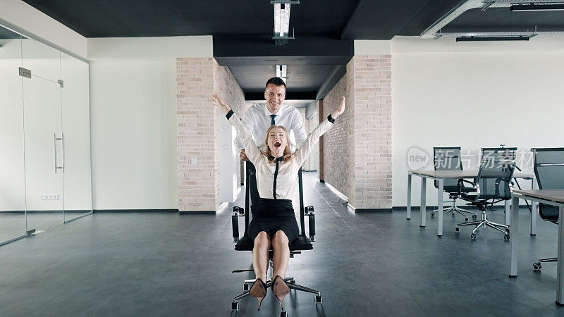 男员工把女同事推到滚轮椅上，在办公室玩得很开心