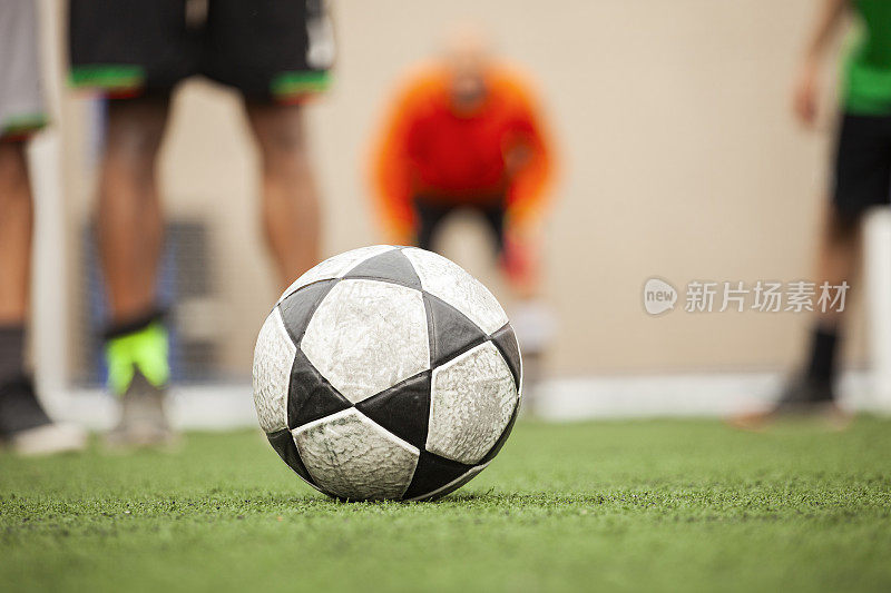足球躺在球场的草坪上，背景是足球运动员和守门员