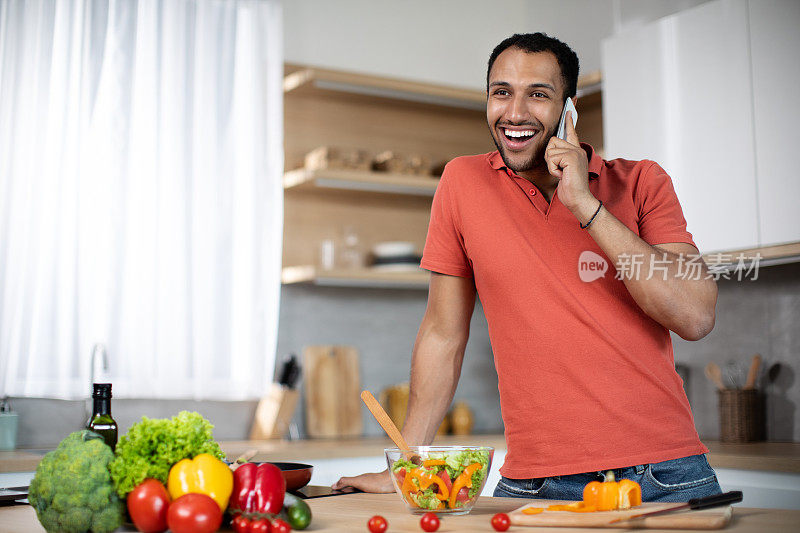 千禧一代非洲裔美国人微笑着用有机蔬菜准备沙拉，用智能手机说话