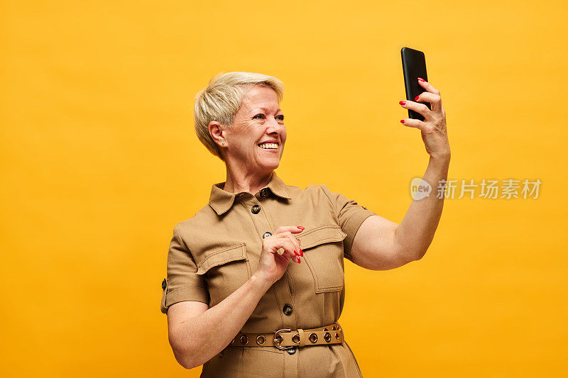 开朗的金发女人在时尚米色连衣裙看着智能手机屏幕