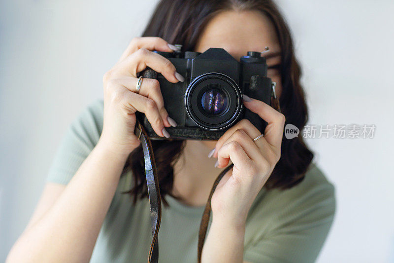 年轻的黑发女子摄影师在室内拍照，在拍照期间看着镜头