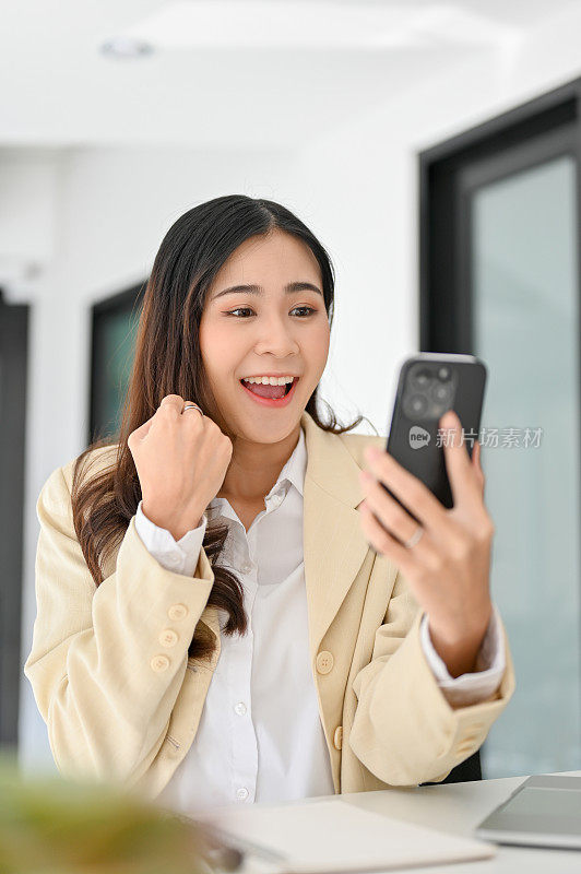 高兴和兴奋的亚洲女商人看着她的手机屏幕，收到好消息