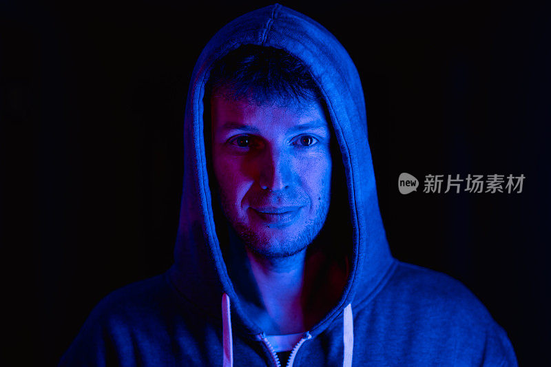 男性肖像在霓虹灯彩灯室内，男性穿着时尚卫衣。红色，蓝色，粉色和紫色。照片与未来主义的人，赛博朋克风格的概念。看镜头的人