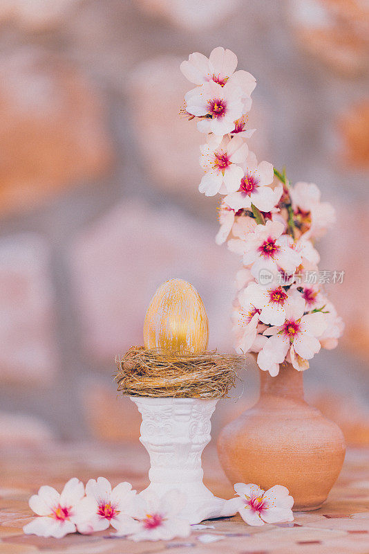 静物画的是一个金色的复活节彩蛋，在一个金色的窝里，在一个白色的柱子上，在一个老桌子上，有杏仁花