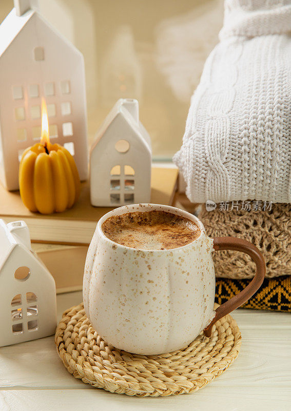 秋天的构图，一杯热咖啡，蜡烛，烛台，一个微型房子和一件温暖的毛衣放在木桌上。应季，早晨热咖啡。放松和静物概念。舒适的室内装饰