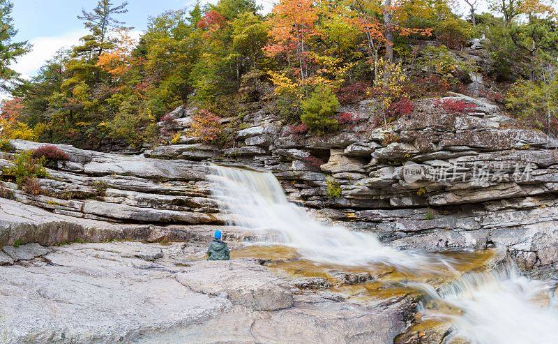 一个孩子在被天然岩石环绕的壮观瀑布旁享受宁静的时刻