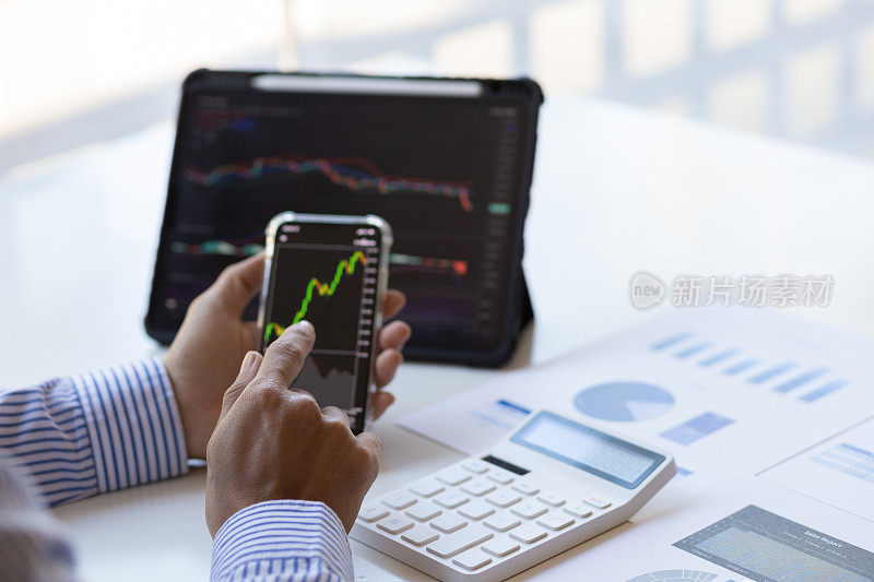 商人工作在平板电脑和智能手机分析股票市场投资图表。投资者在移动和平板电脑应用程序上分析股市和外汇交易图表数据。