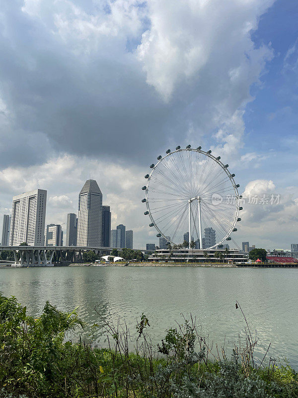 新加坡摩天轮的图像，阳光明媚，多云的蓝天为背景，城市海滨景观，摩天大楼，重点在前景