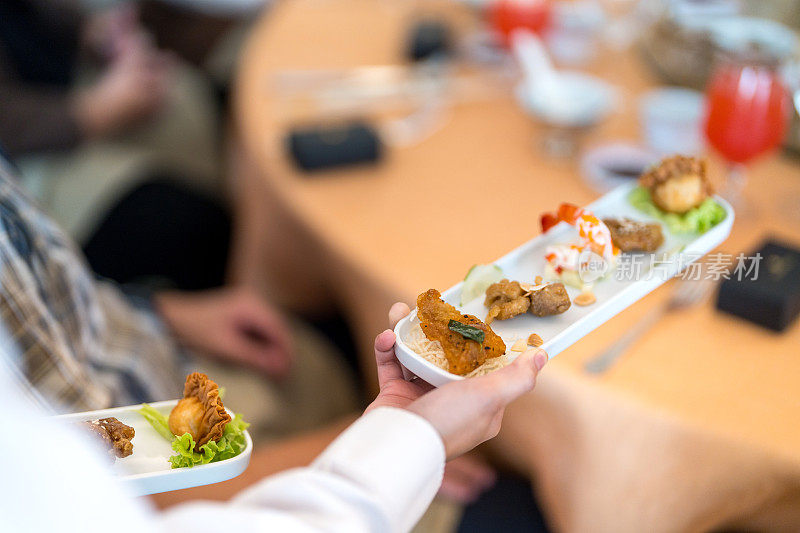 在节日活动、聚会或婚宴上，服务员熟练地端着盛满食物的盘子。软焦点图像。