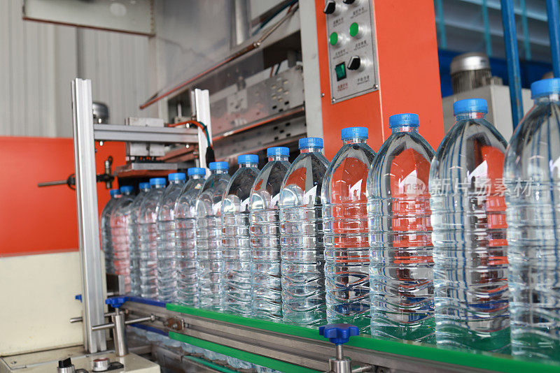 在一家饮用水工厂，用塑料瓶装瓶饮料的生产线在一个干净的带式输送机上