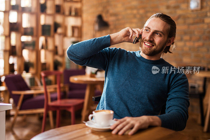 微笑的年轻男子在咖啡馆里讲手机。