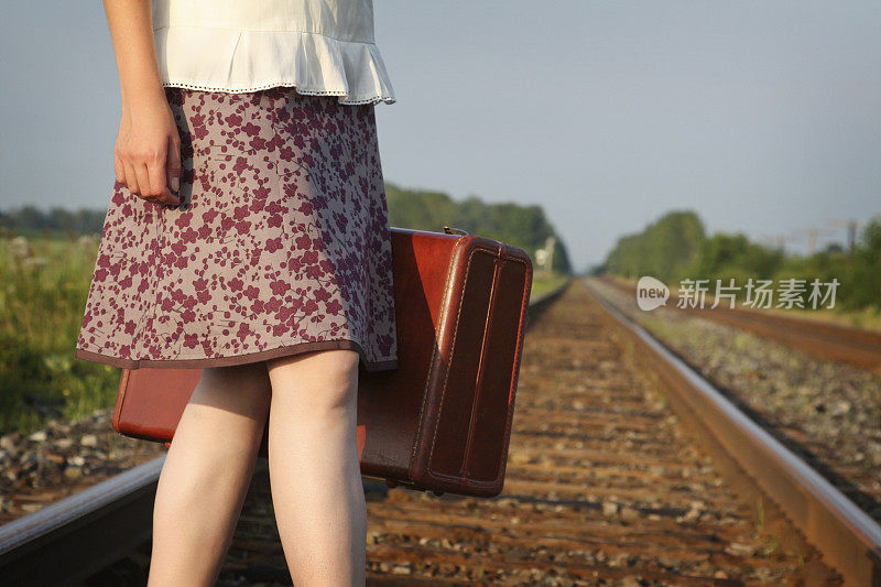 一个女人提着一个手提箱穿越铁轨