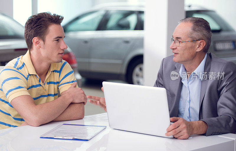 成熟的汽车销售人员在汽车经销商与客户交谈。