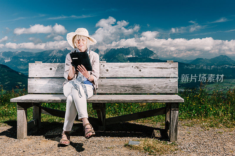 在阿尔卑斯的长凳上拿着平板电脑的资深女性