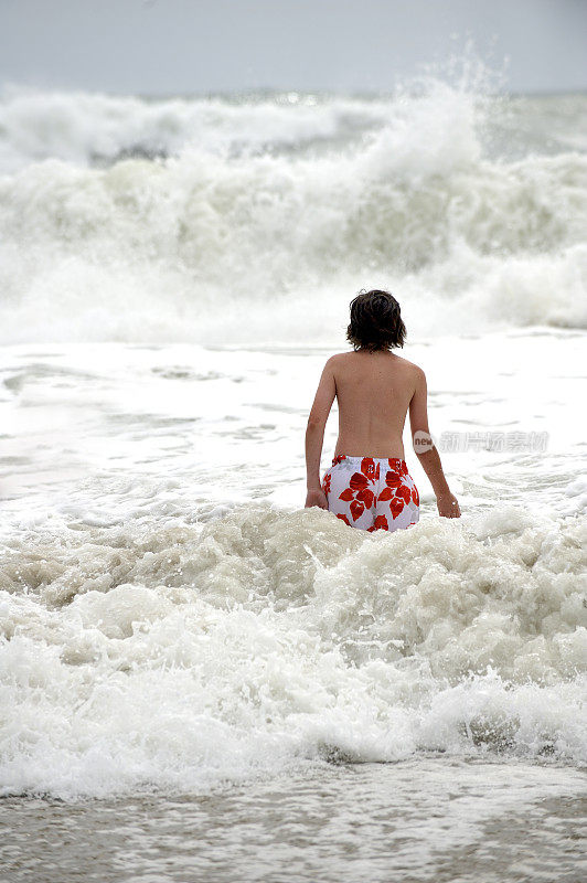 年轻的男孩在大海里，一个巨大的波浪接近