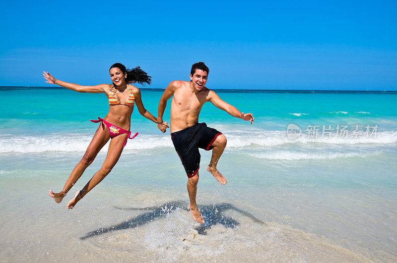年轻幸福的夫妇在热带海滩手拉手跳