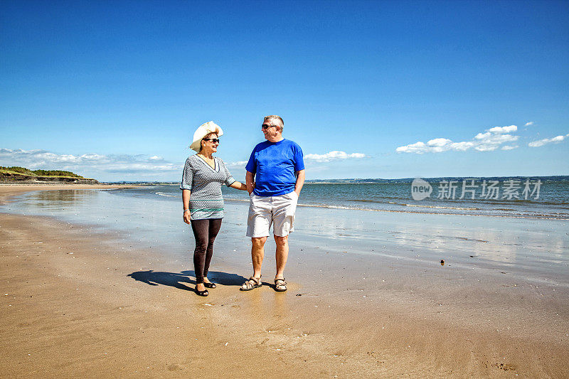 一对成熟的微笑情侣在海滩上散步