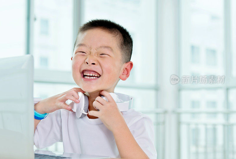 年轻的亚洲男孩戴着耳机使用笔记本电脑