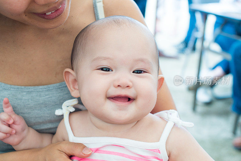 微笑的婴儿坐在她妈妈的膝盖上