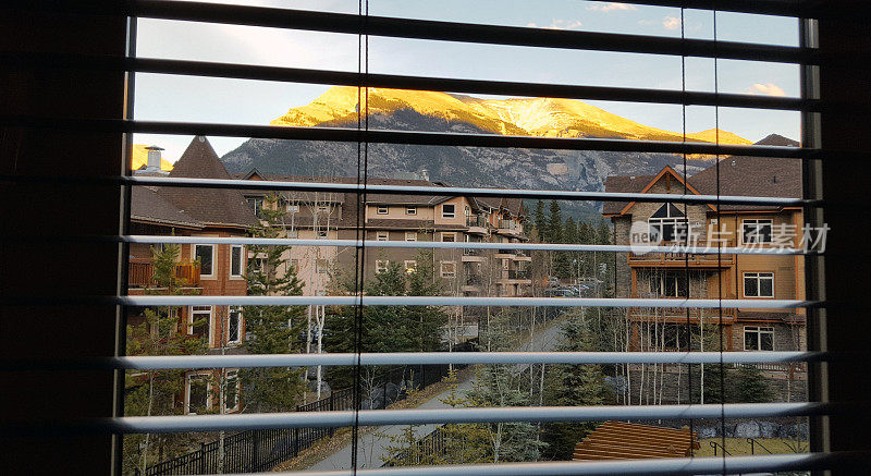 透过百叶窗看阳光下的山脉和公寓