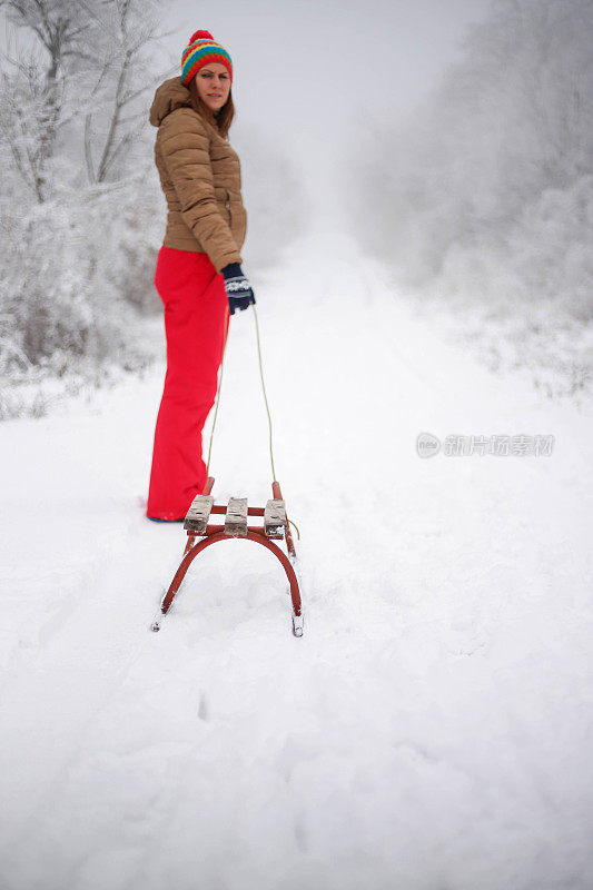 女孩在森林里散步，拉雪橇。一个开心的女人。圣诞假期。女孩免费休息。圣诞树躺在雪橇上。美丽的年轻女孩或女人在森林里散步。拉木制雪橇