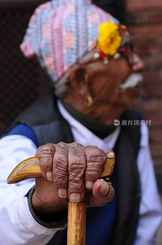 坐着的尼泊尔老人，穿着传统服装，拄着拐杖