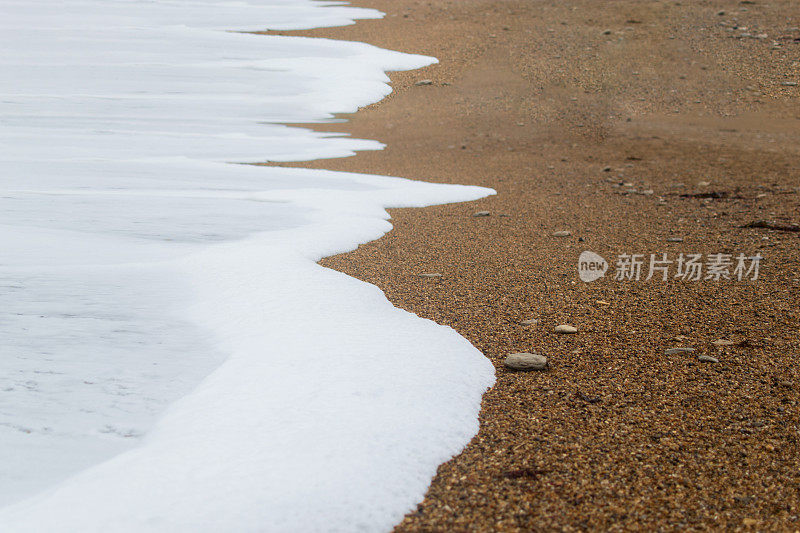 柔软的泡沫被海水留在布满卵石的海滩上