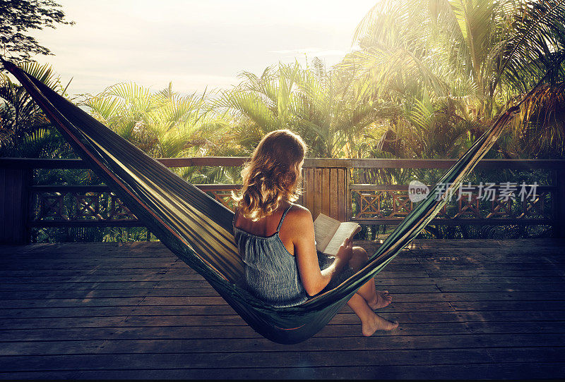 日落时分，在丛林的吊床上，一个穿着礼服的女人在看书。