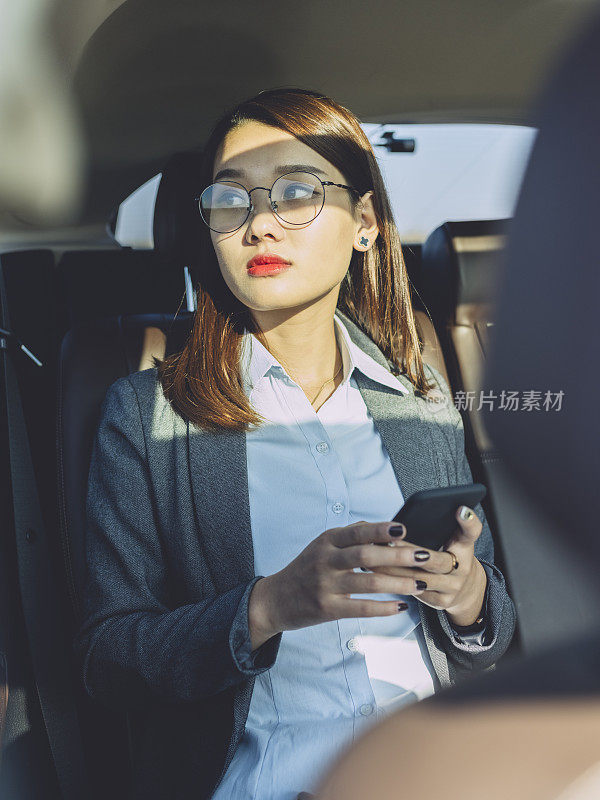 年轻女商人在汽车后座上用手机