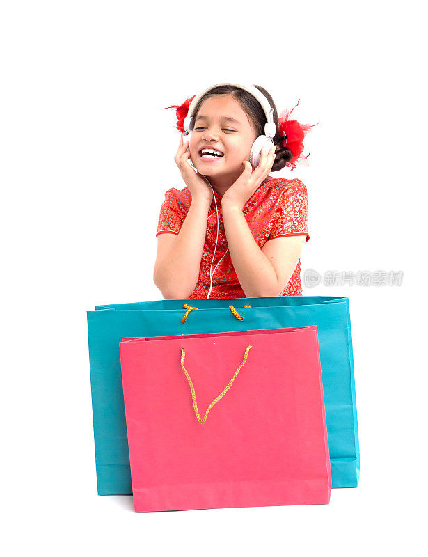 农历新年亚洲小孩女人旗袍概念，孤立一个女孩穿着红色连衣裙和耳机坐在购物袋