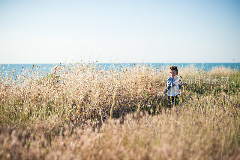 快乐的小男孩奔跑在金色的麦田里，背景是大海