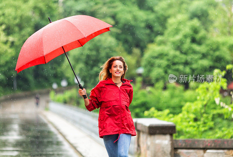 快乐的年轻女子撑着雨伞在雨中行走