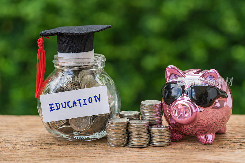 玻璃罐里装满硬币和毕业生帽子标签与Piggybank和硬币堆叠作为教育，教育或储蓄的概念