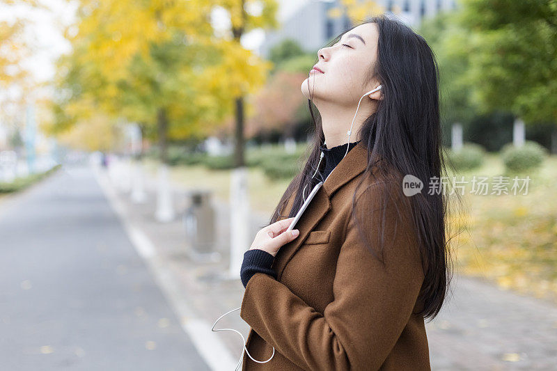 一个年轻女子在秋天的街上听音乐