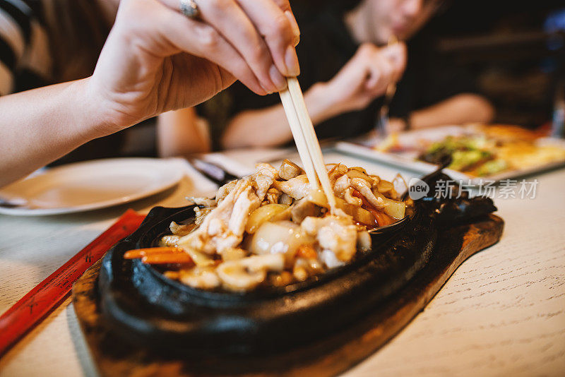 近距离观看女性手握肉在筷子，而吃中国菜在餐厅。