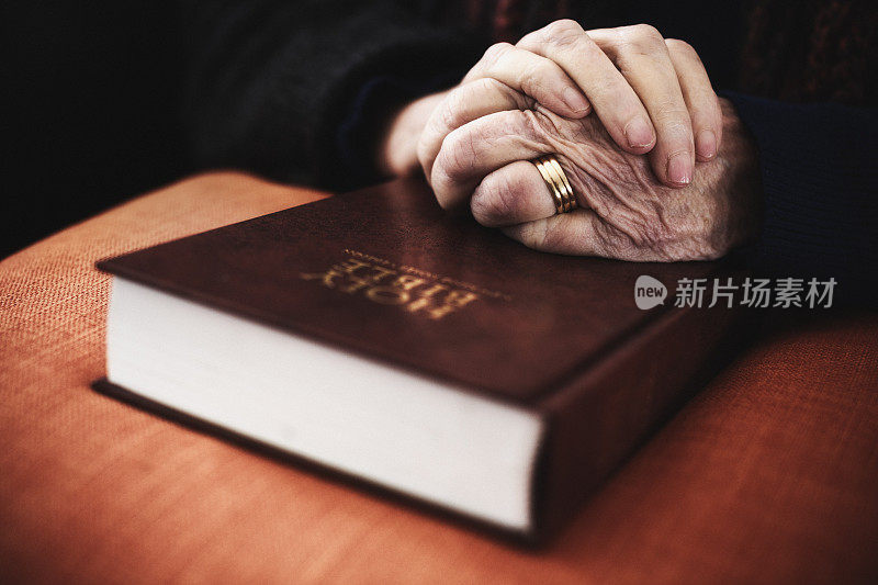 老妇人双手合十在圣经上祈祷