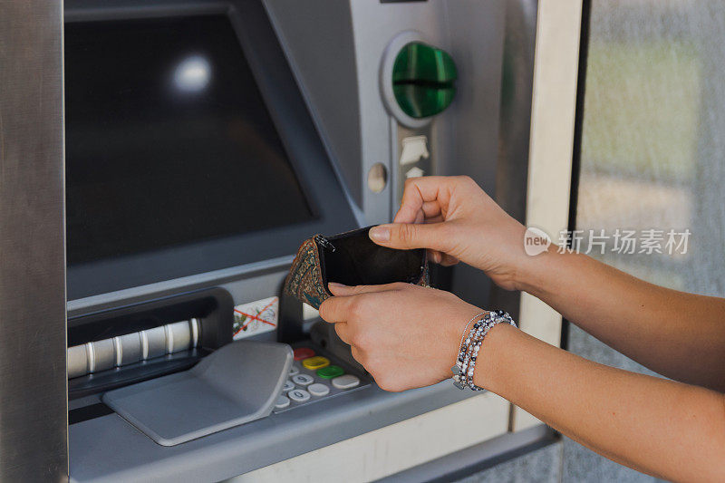 在自动取款机旁拿着空钱包的女人。破产的概念