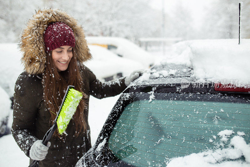 年轻女子在清理车上的积雪