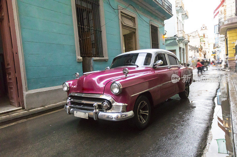 一辆粉色复古车行驶在古巴的街道上