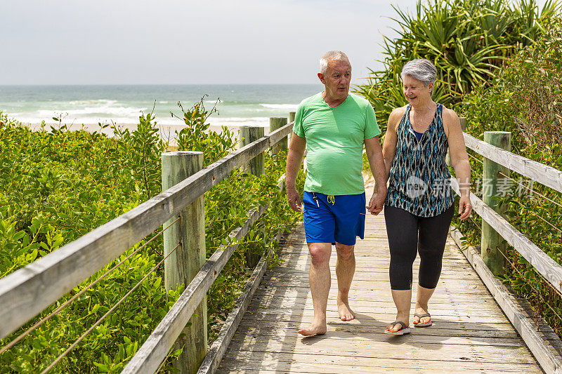 一对老年夫妇在海滩的木板路上散步