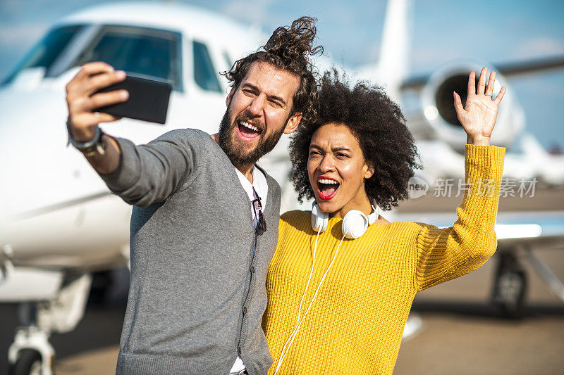 富有的非洲裔美国女孩挥手，与她的伴侣在一架停在机场跑道上的私人飞机旁自拍