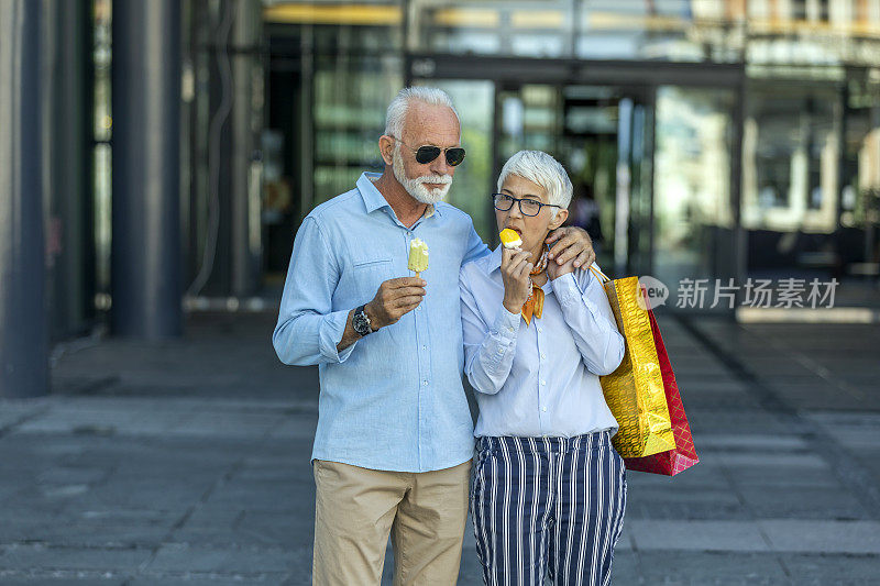 成熟的夫妇走在城市的大街上，在成功购物后吃冰淇淋