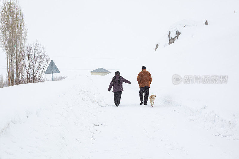 一对老年夫妇在下雪的乡村路上穿着暖和的衣服