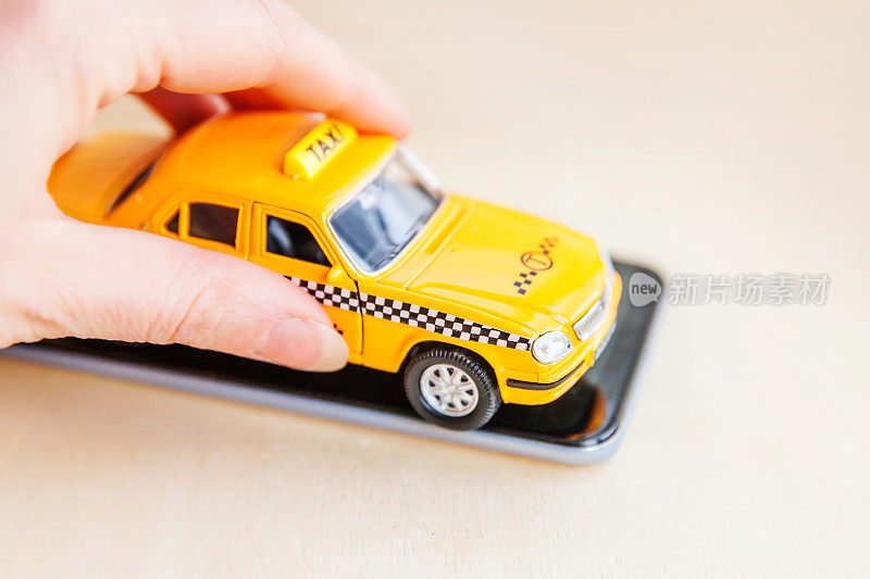 智能手机出租车服务应用的在线搜索、呼叫和预约出租车的概念。手握黄色玩具车出租车在空屏幕上智能手机木制背景。出租车的象征