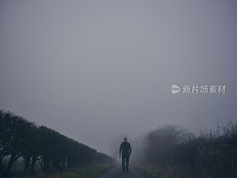 一个人在阴沉的冬日大雾中走在乡间小路上。