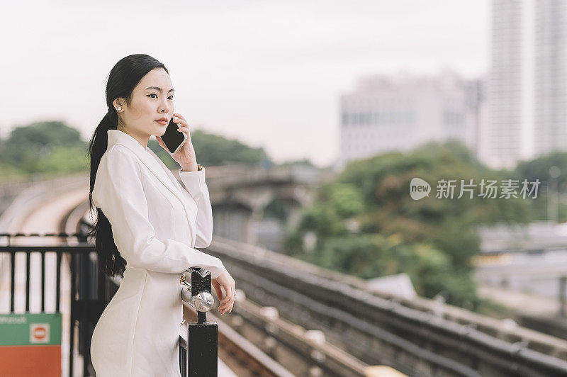 一位年轻的亚洲华裔女商人在单轨火车站边走边听着智能手机