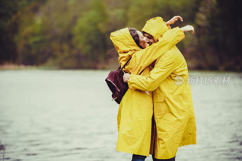 拥抱一对穿着雨衣在雨中徒步旅行的情侣