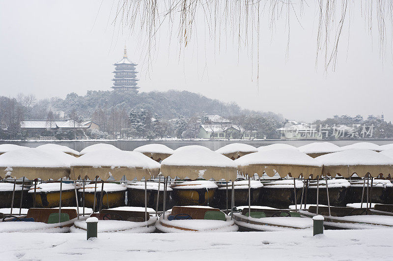 在杭州西湖的冬雪中，雷峰塔矗立在停泊的游船后面