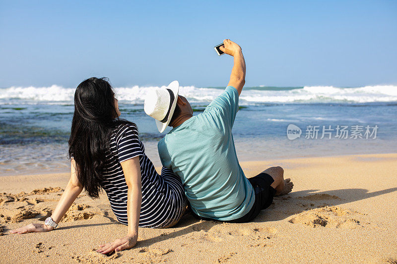 一对亚洲年轻夫妇坐在海滩上遥望远方