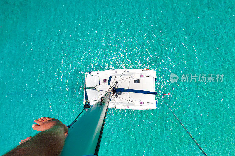 在双体船桅杆上的人向下看热带水域
